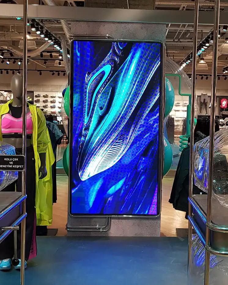 Pantalla LED vertical mostrando contenido gráfico dentro de una tienda de ropa deportiva.