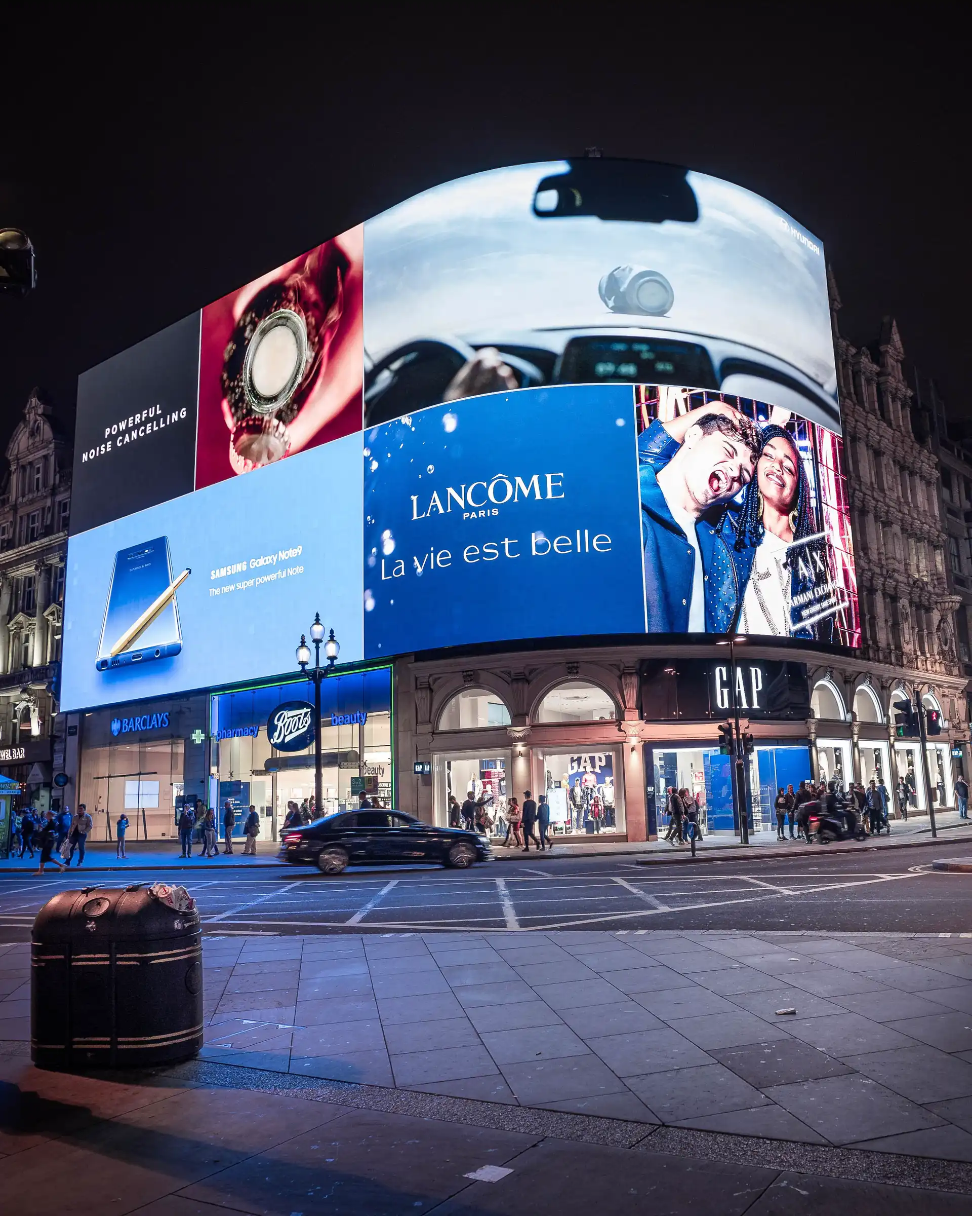 Pantallas LED de gran formato en un cruce comercial de la ciudad, exhibiendo anuncios de marcas como Lancôme.