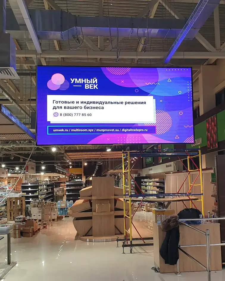 Pantalla LED suspendida en una tienda comercial, mostrando anuncios de servicios personalizados.