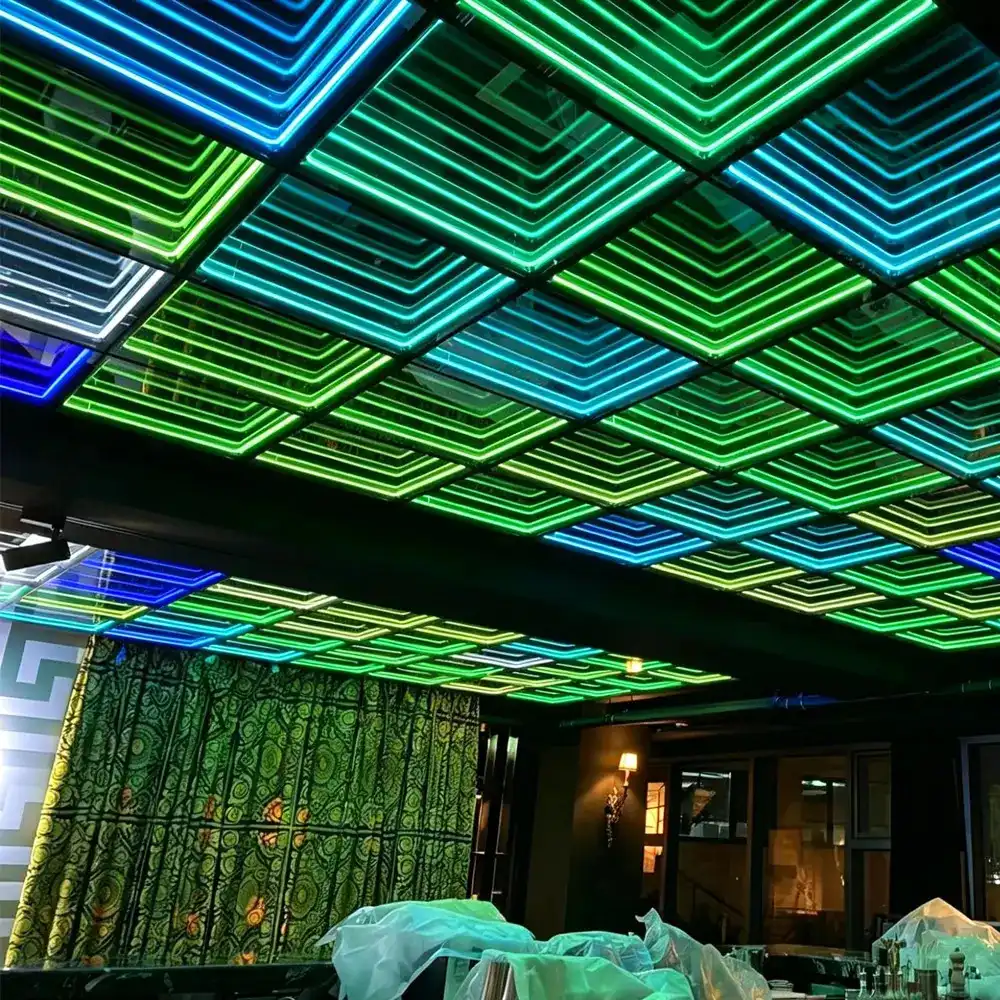 Techo de un restaurante cubierto con paneles LED Espejo Infinito 3D en tonos verde y azul, creando un efecto de profundidad geométrica sobre las mesas.