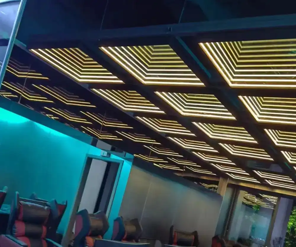 Pérgola con techo de paneles LED Espejo Infinito 3D en tono dorado Techo de una pérgola exterior revestido con paneles LED Espejo Infinito 3D en color dorado, iluminando una zona de asientos tipo gaming.