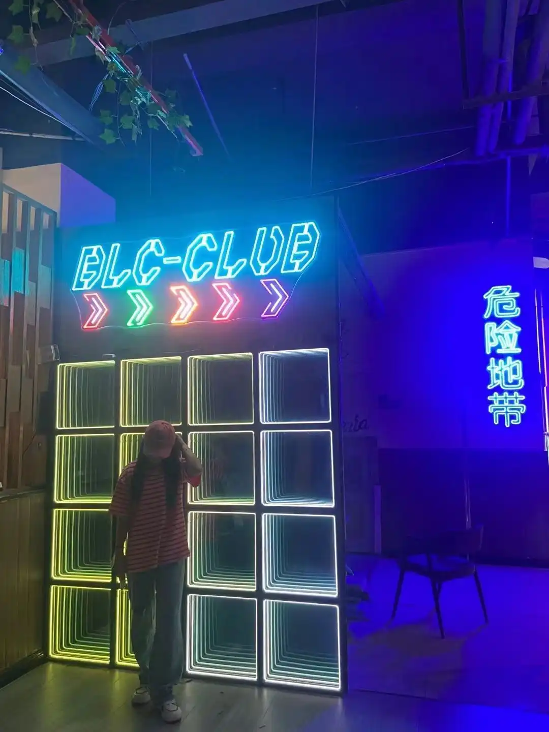 Pared LED Espejo Infinito 3D combinada con letrero de neón BLC-CLUB Pared de paneles LED Espejo Infinito 3D en tonos verde, azul y blanco junto a un letrero de neón BLC-CLUB con flechas de colores.