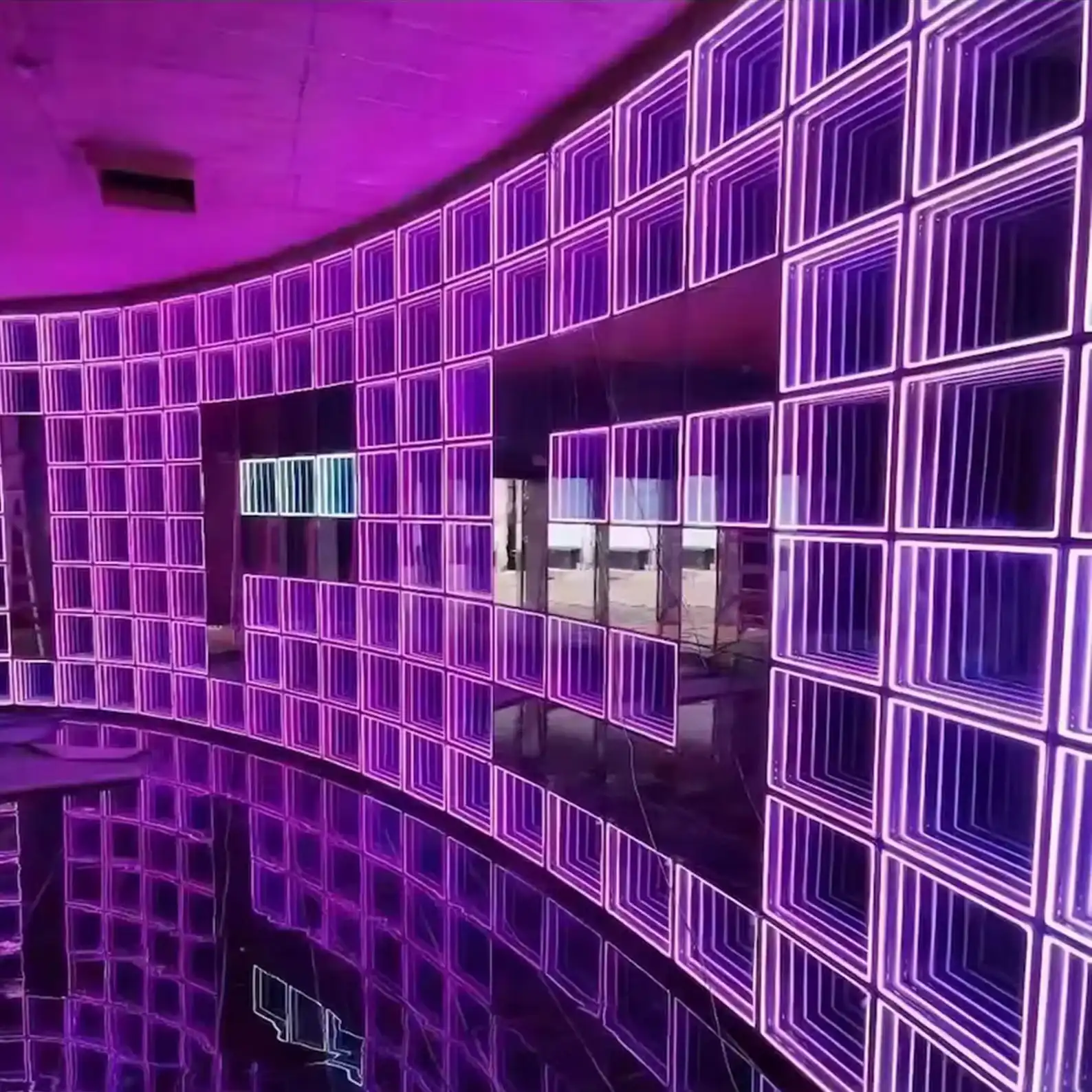 Muro curvo de gran formato revestido con decenas de paneles LED Espejo Infinito 3D en tono púrpura, instalado en un espacio circular de doble altura.