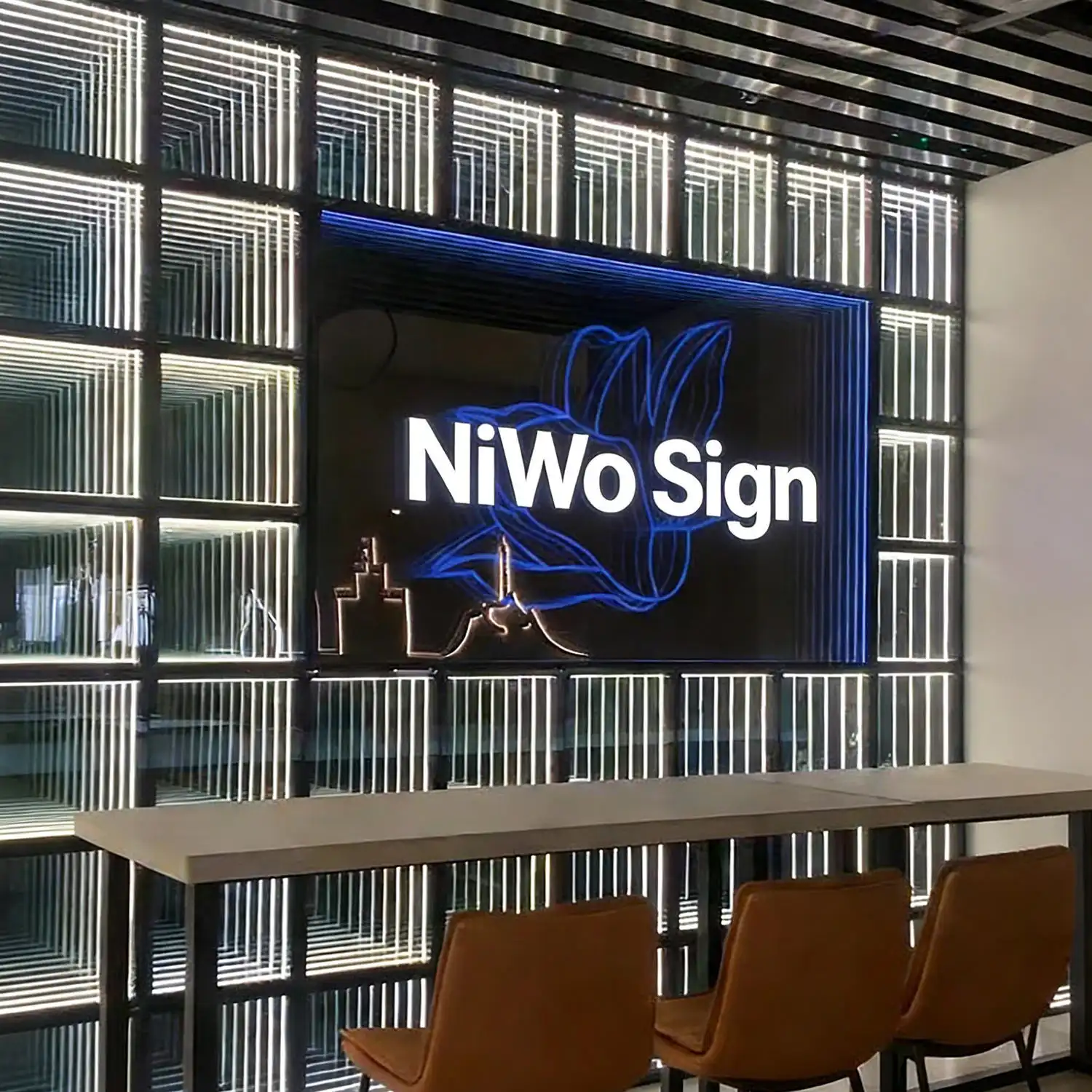 Pared LED Espejo Infinito 3D blanca junto a letrero corporativo NiWo Sign Pared de paneles LED Espejo Infinito 3D en tono blanco frío junto a un letrero retroiluminado NiWo Sign, en una zona de mesas altas.