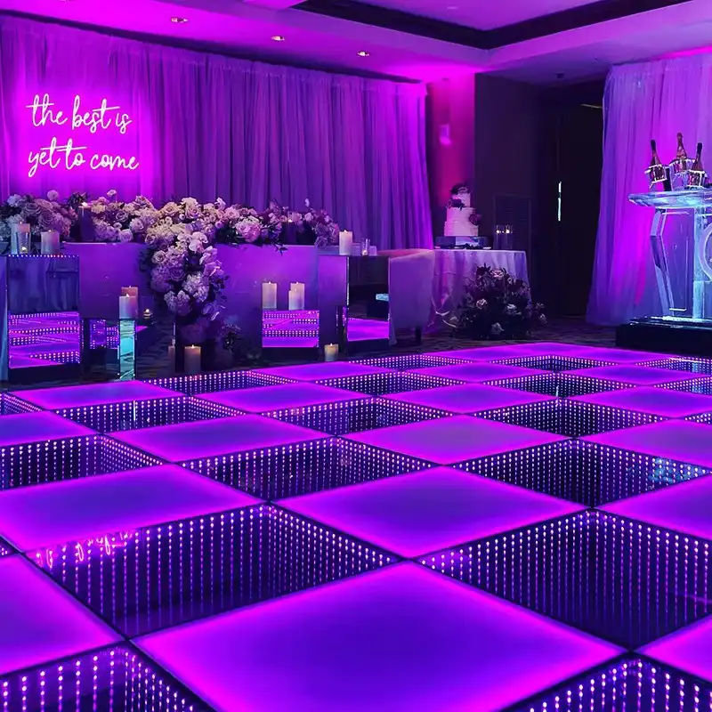 Pista LED 3D Infinity Mirror púrpura en boda junto al letrero The best is yet to come Pista de baile LED 3D Infinity Mirror en tono púrpura junto al letrero de neón The best is yet to come, con decoración floral de boda y velas.