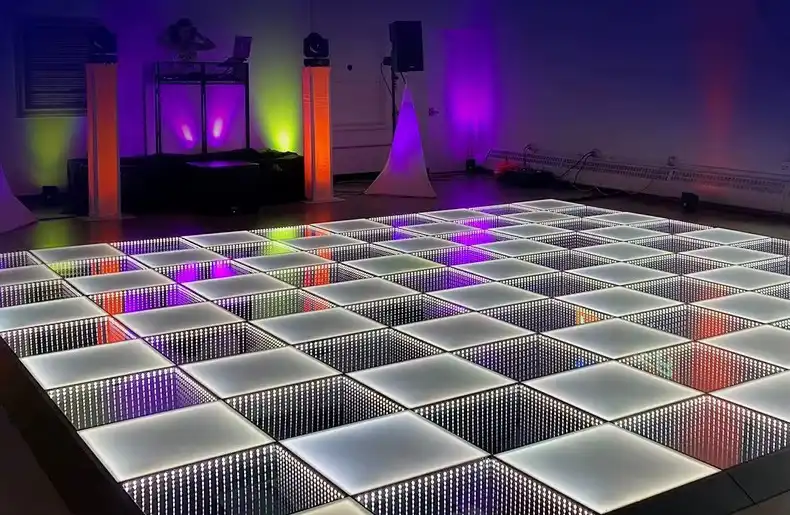 Pista LED 3D Infinity Mirror blanca junto a la cabina de DJ Pista de baile LED 3D Infinity Mirror en tono blanco cálido junto a la cabina de DJ, con invitados bailando en movimiento.