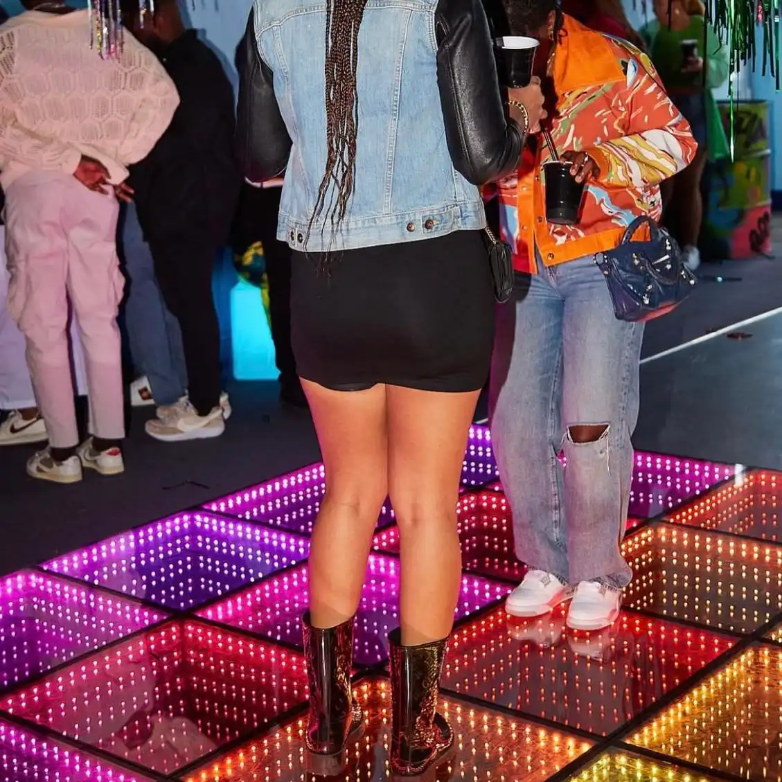 Invitados bailando de cerca sobre la pista LED 3D Infinity Mirror multicolor Detalle de invitados bailando muy de cerca sobre la pista de baile LED 3D Infinity Mirror en tonos púrpura, rosa y naranja durante una fiesta.