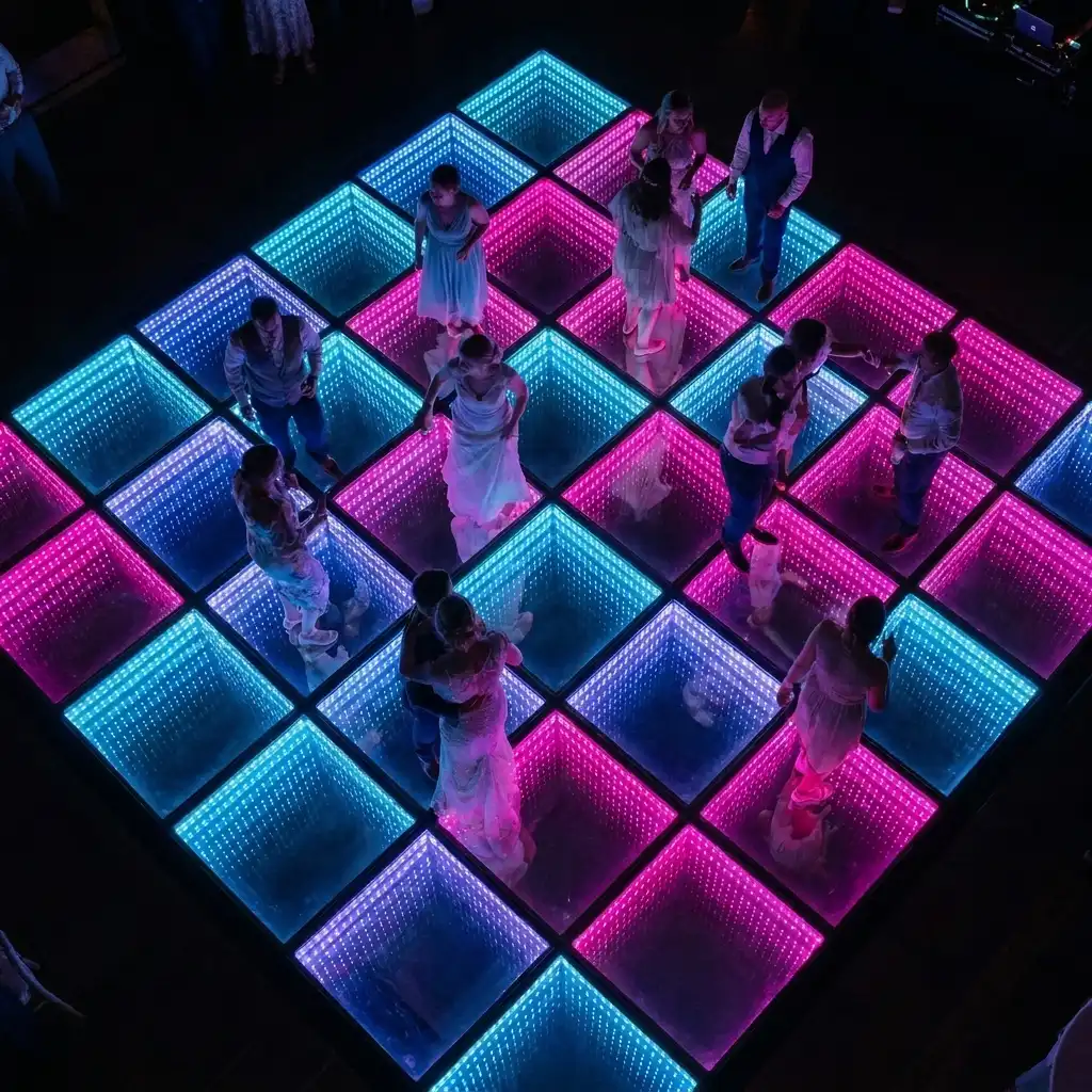 Vista aérea de una boda sobre la pista LED 3D Infinity Mirror Vista aérea de los novios e invitados bailando sobre la pista de baile LED 3D Infinity Mirror en tonos rosa, azul y púrpura durante la recepción de la boda.