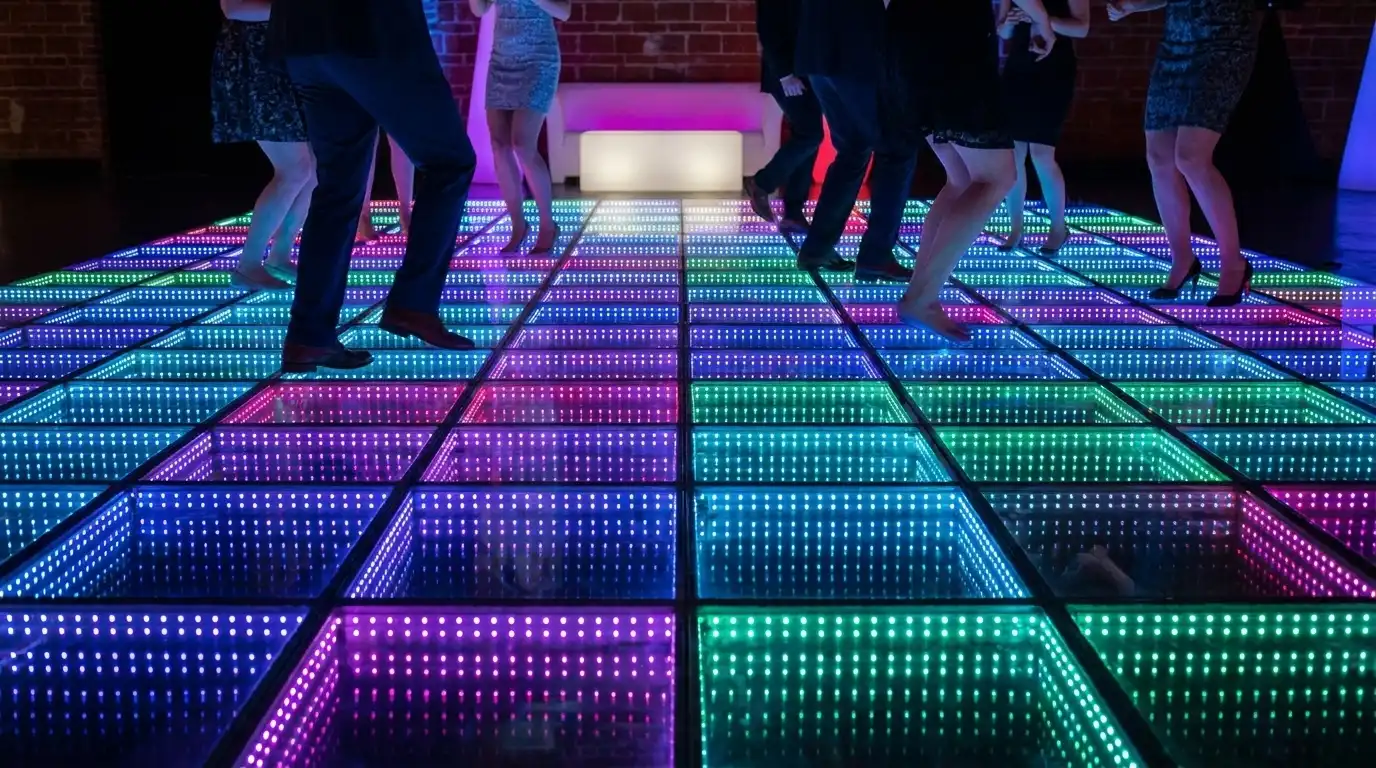 Invitados bailando sobre la pista LED 3D Infinity Mirror junto a una pared de ladrillo Vista de las piernas de los invitados bailando sobre la pista de baile LED 3D Infinity Mirror multicolor, junto a una pared de ladrillo y mobiliario lounge.