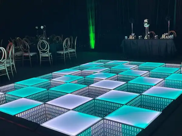 Pista LED 3D Infinity Mirror turquesa en la recepción de una boda Pista de baile LED 3D Infinity Mirror en tono turquesa junto a la mesa de novios Mr & Mrs, en un salón de recepción de boda con centros de mesa florales.