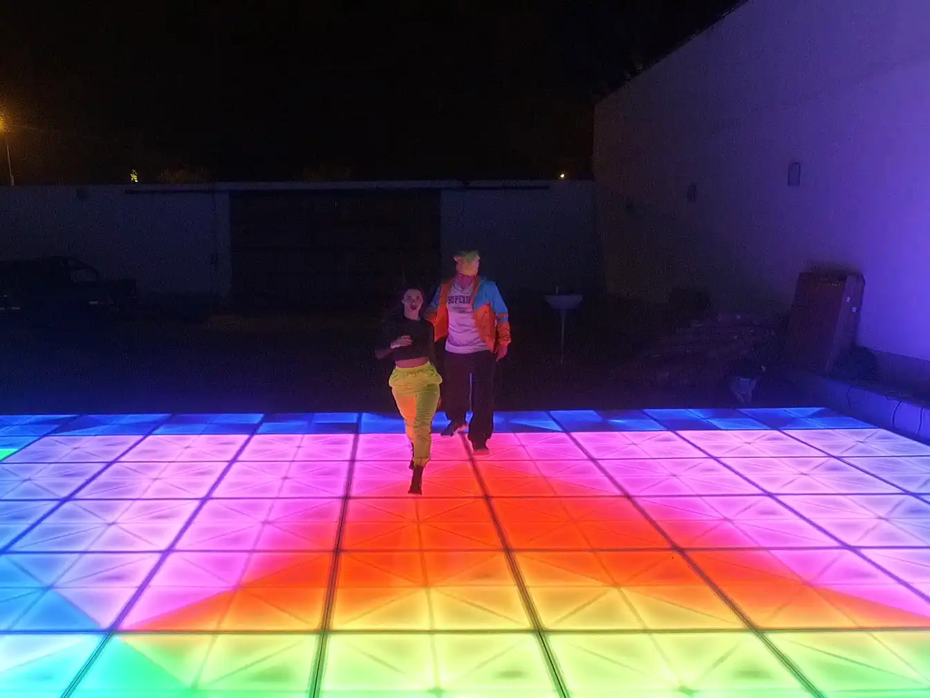 Dos personas bailando sobre una pista de baile LED con iluminación en tonos vibrantes de naranja y púrpura, ideal para eventos al aire libre.