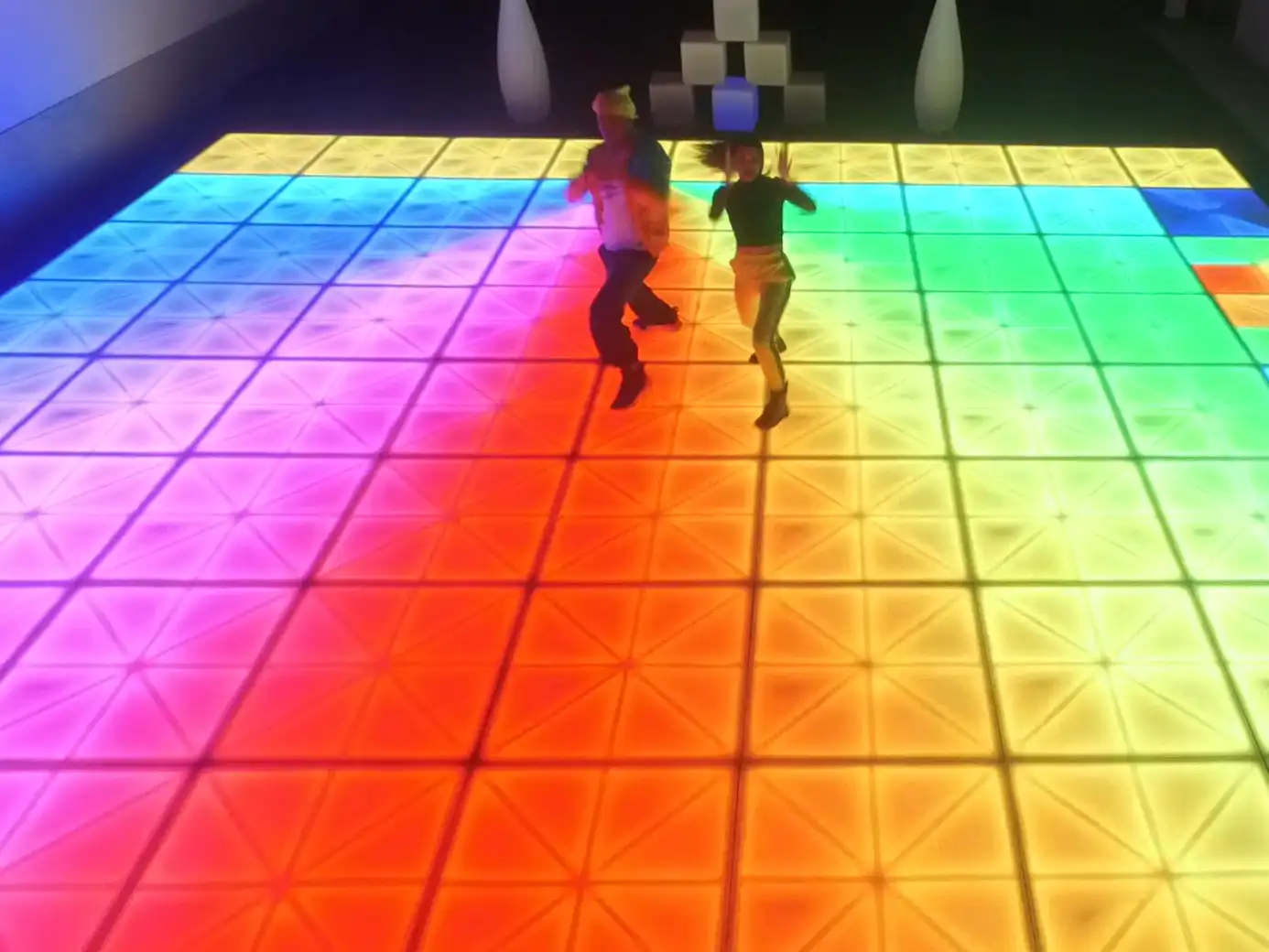 Dos personas bailando en una pista de baile LED con efectos de iluminación en tonos rojos y naranjas, ideal para eventos sociales.