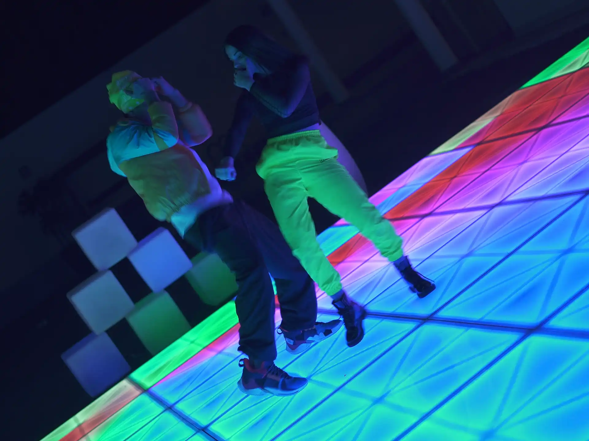 Pareja bailando en una pista de baile LED con efectos de luces multicolores en tonos vibrantes, creando una atmósfera animada.