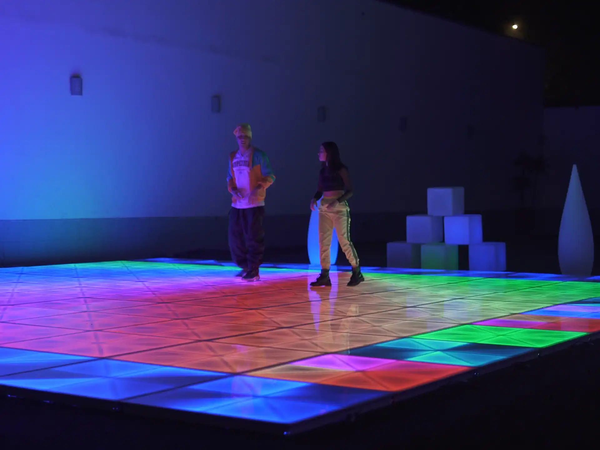 Dos personas bailando en una pista de baile LED con efectos de luz en tonos vibrantes de verde, rojo y azul, ideal para eventos al aire libre.