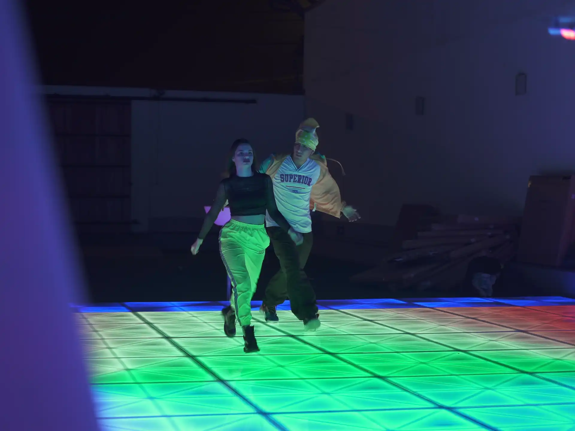 Dos personas disfrutando de una pista de baile LED con iluminación verde y azul, perfecta para eventos nocturnos llenos de energía.