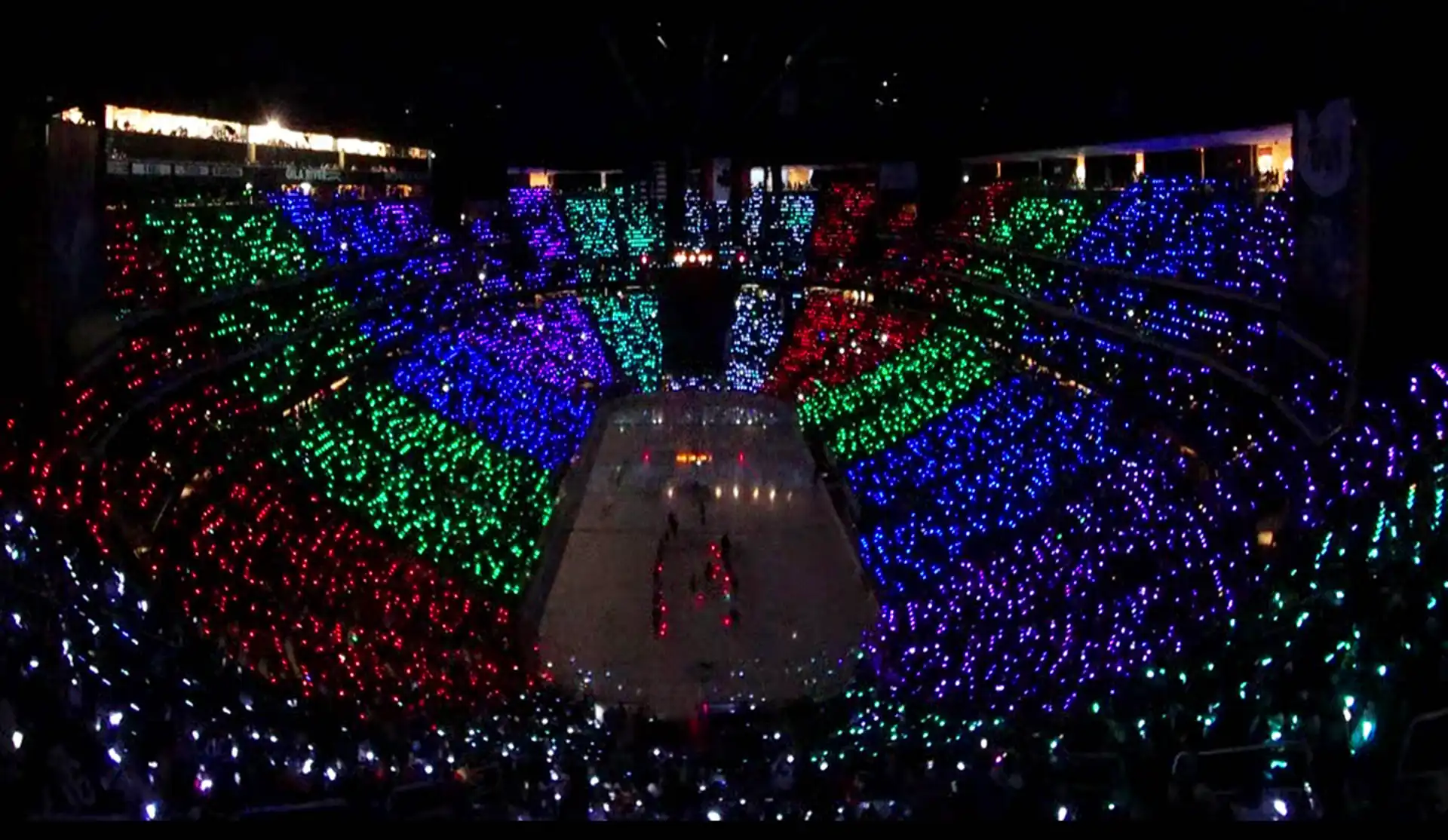 Estadio lleno de pulseras LED sincronizadas en múltiples colores, creando un espectáculo visual impresionante.