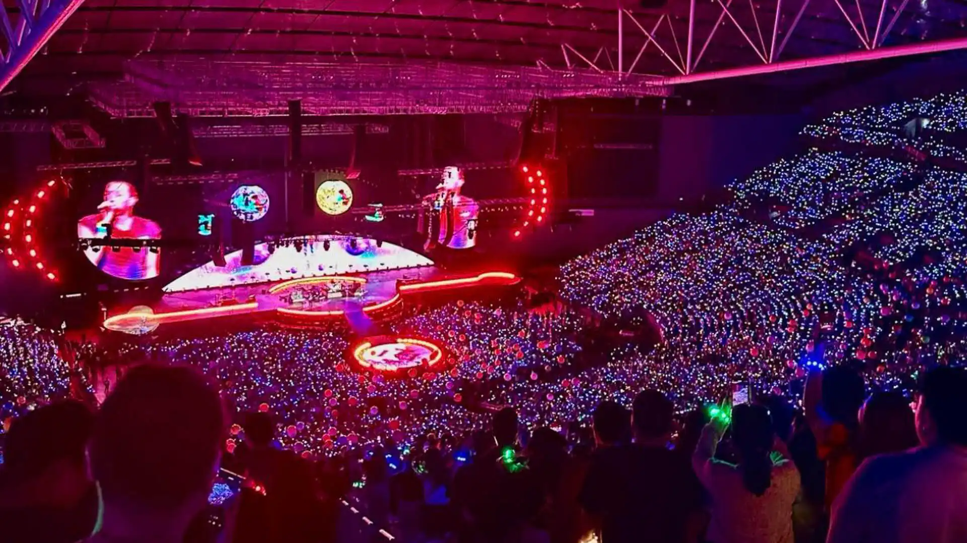 Vista aérea de un concierto masivo con pulseras LED sincronizadas, llenando el estadio de colores brillantes.