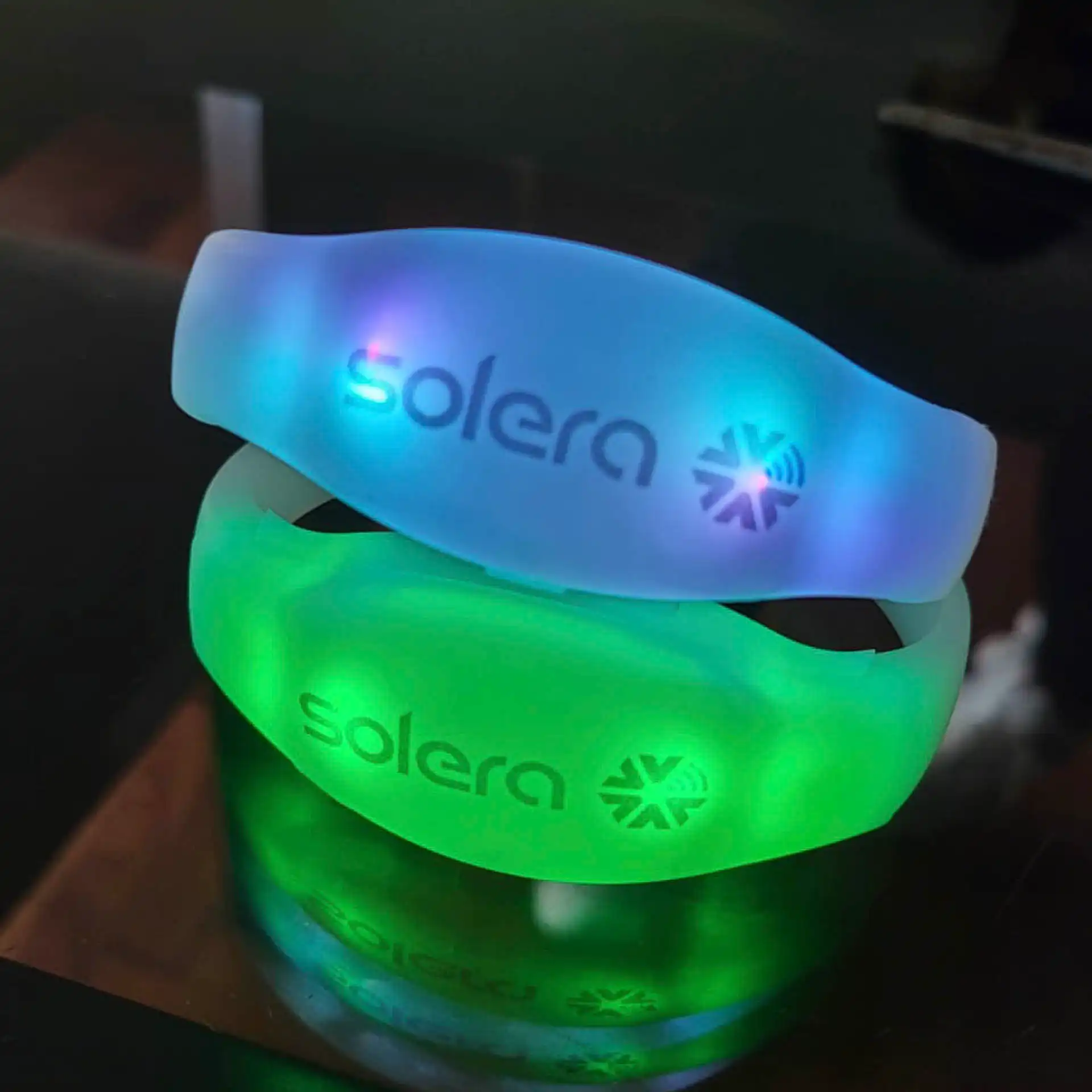 Pulseras LED personalizadas con logotipo Solera, iluminando en colores verde y azul, perfectas para branding en eventos.