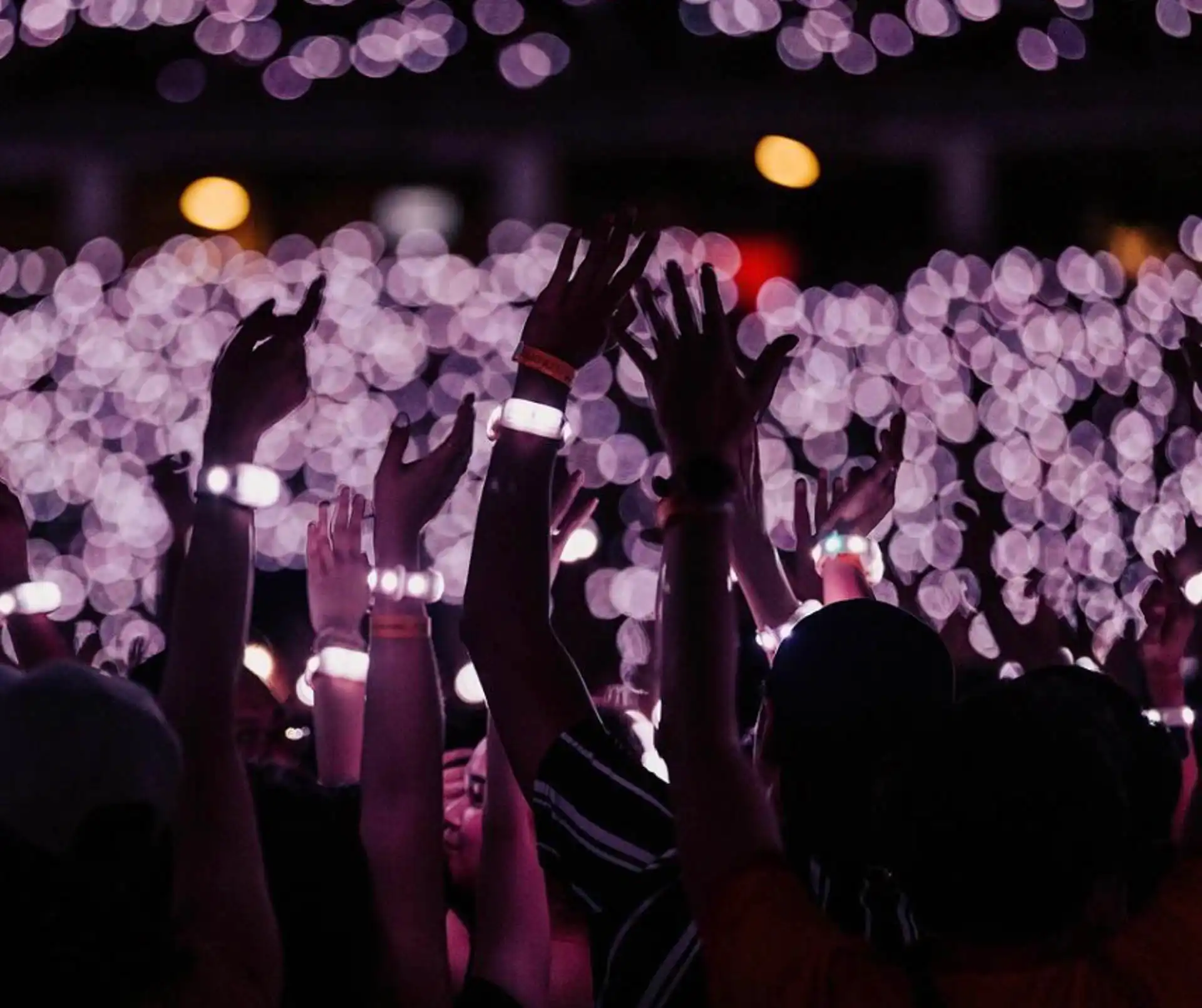 Manos levantadas con pulseras LED inalámbricas brillando en un evento masivo, creando un ambiente único y sincronizado en conciertos y festivales.