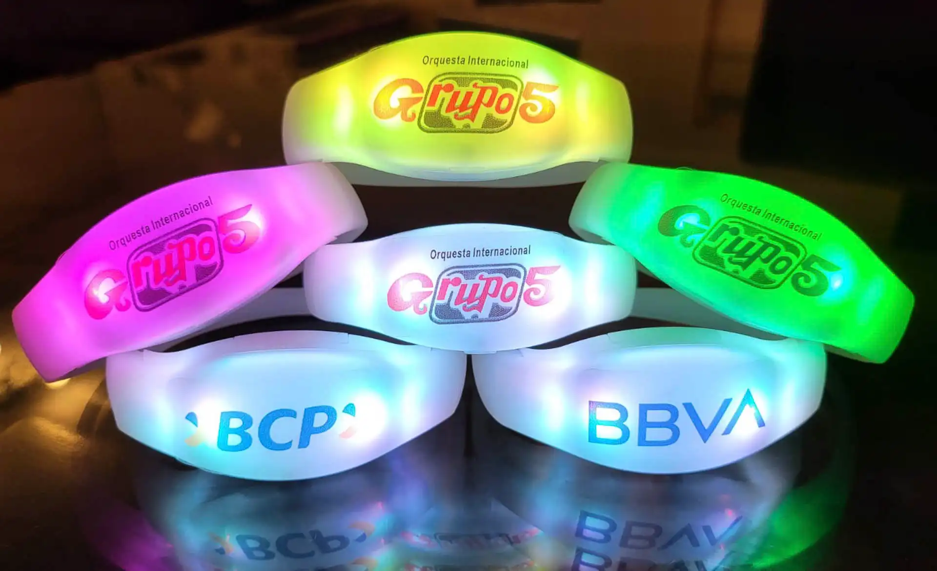 Pulseras LED personalizadas para Grupo 5, BBVA y BCP, iluminando en varios colores durante eventos y conciertos.