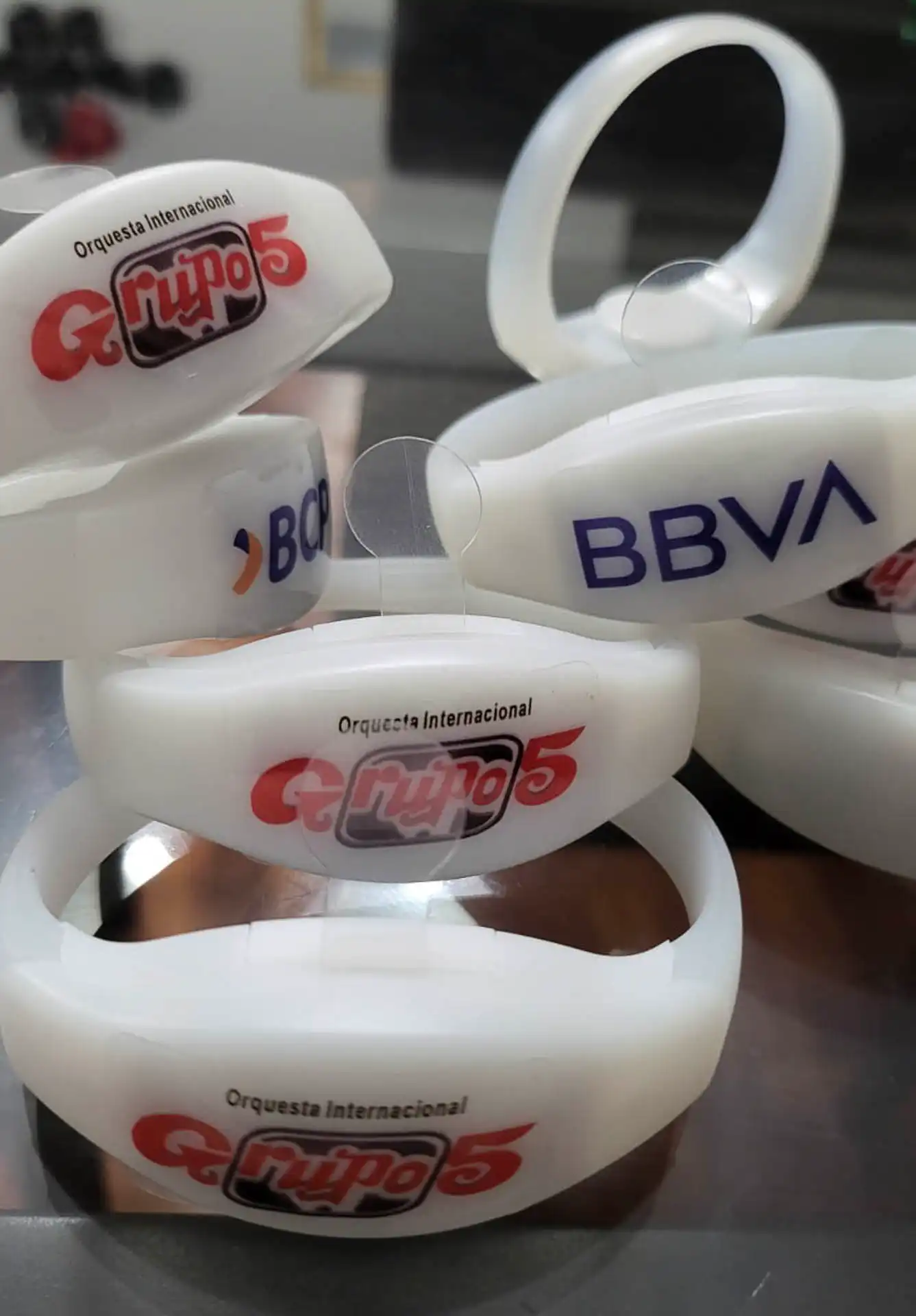 Primer plano de pulseras LED personalizadas con logotipos de Grupo 5, BBVA y BCP, listas para iluminar eventos masivos.