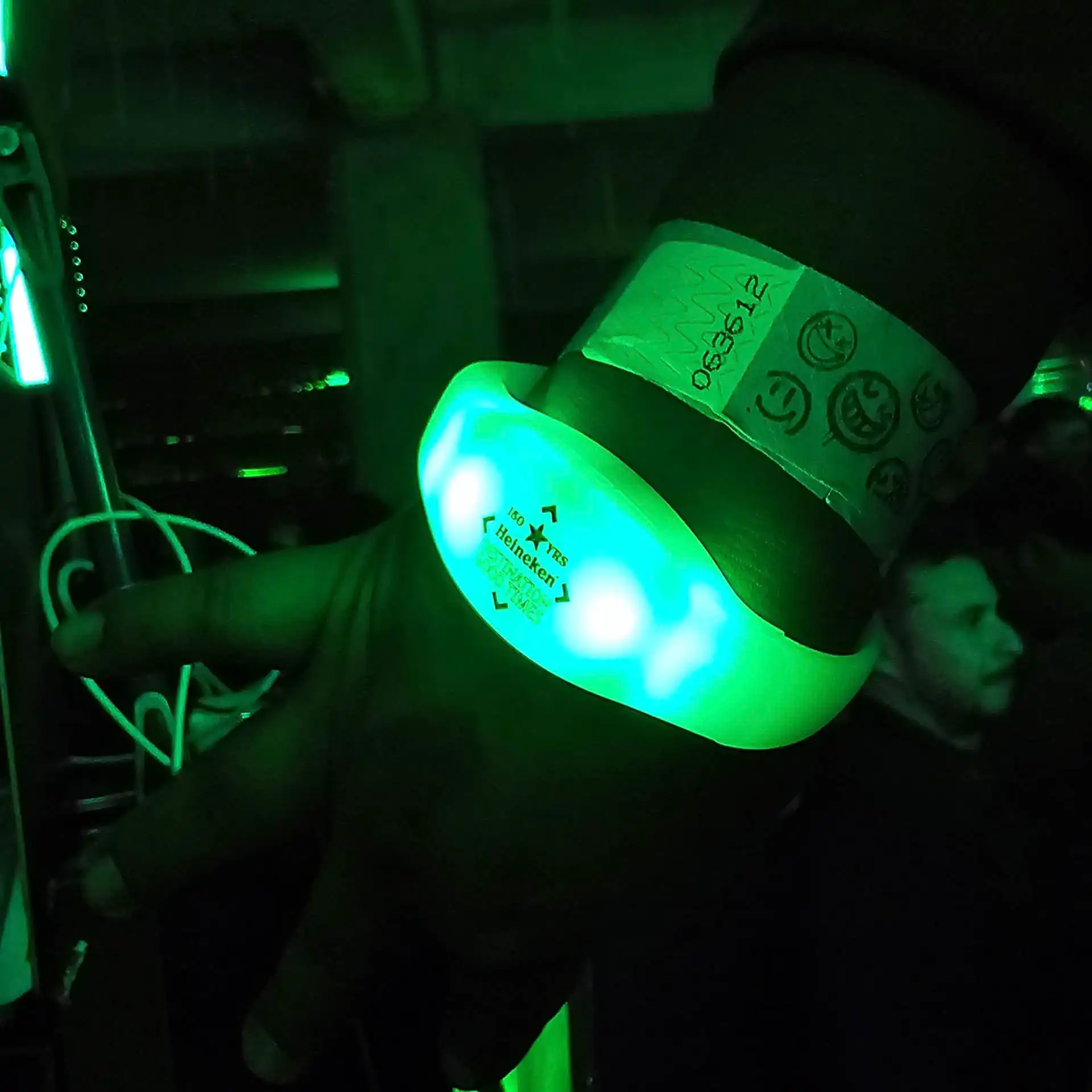 Pulsera LED personalizada con el logotipo de Heineken, iluminada en verde durante una fiesta para interactuar con los asistentes.