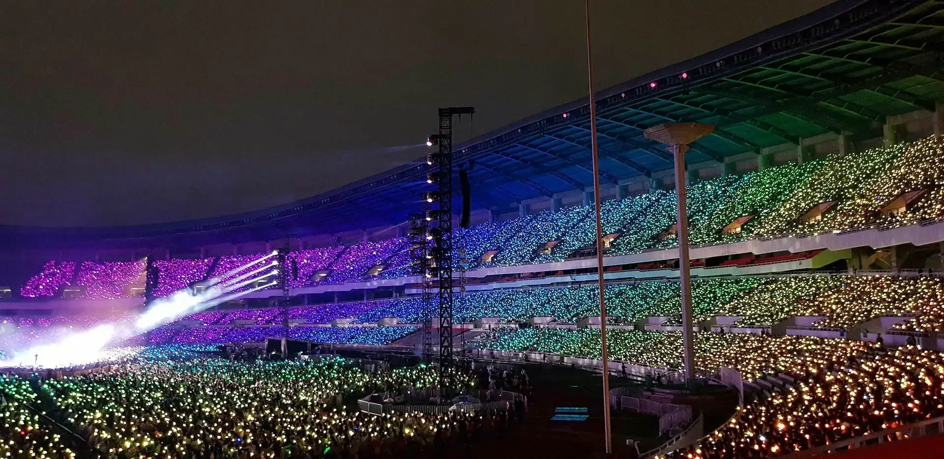 Un estadio lleno de espectadores con pulseras LED iluminadas en múltiples colores formando patrones.