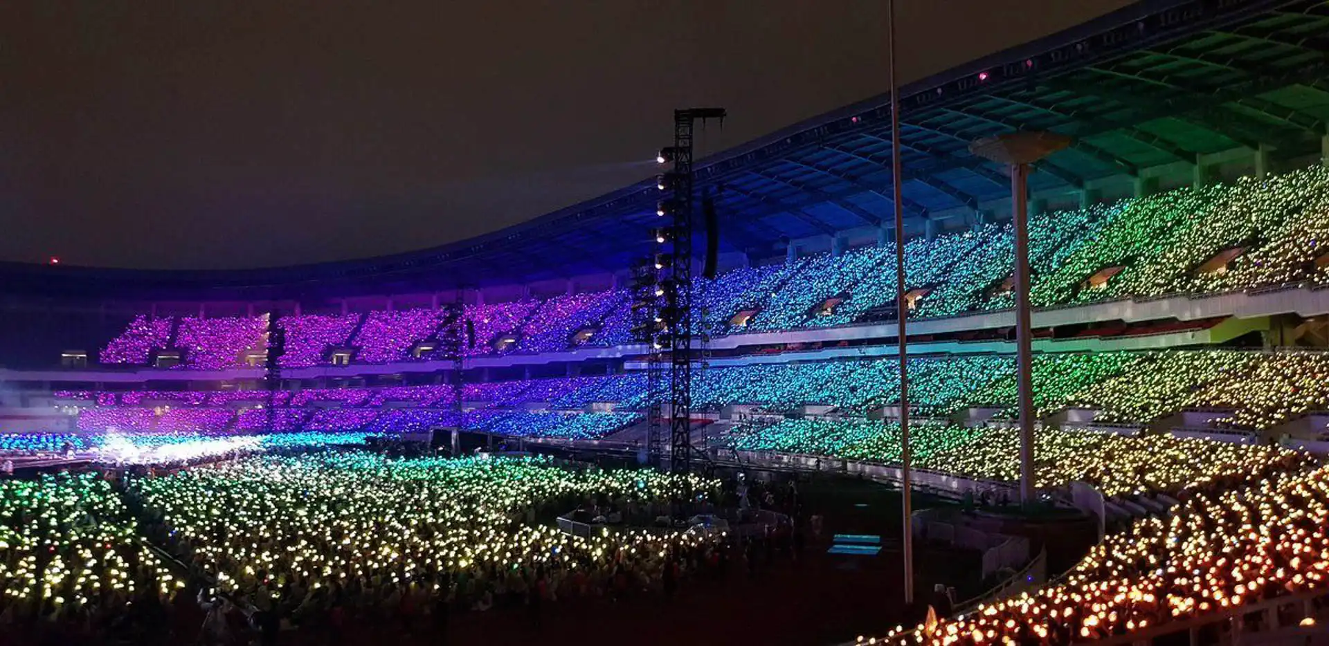 Imagen de un estadio con luces LED multicolor iluminando la multitud durante un concierto nocturno.