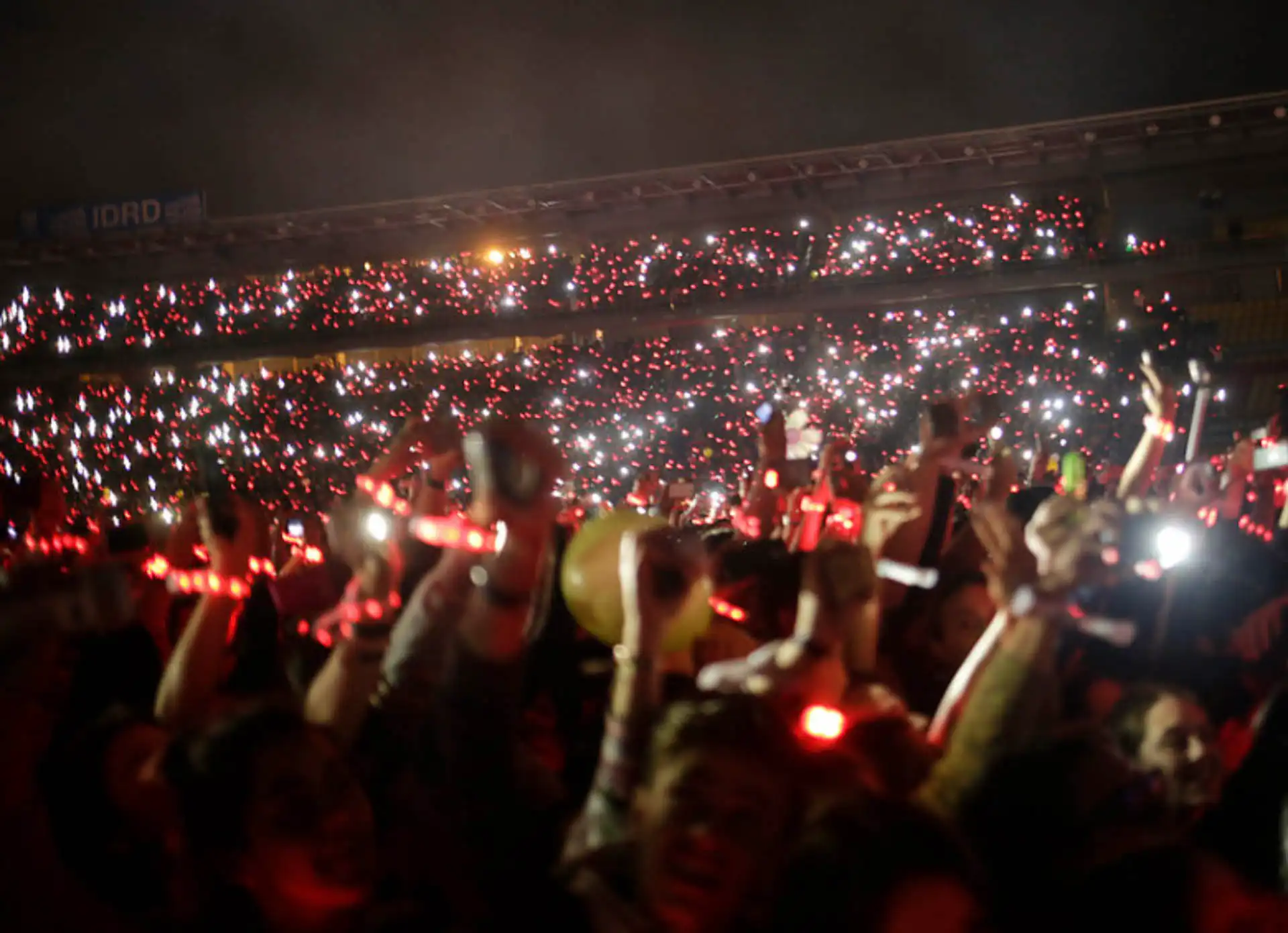 Multitud usando pulseras LED rojas durante un espectáculo, generando una atmósfera vibrante y coordinada en eventos masivos.