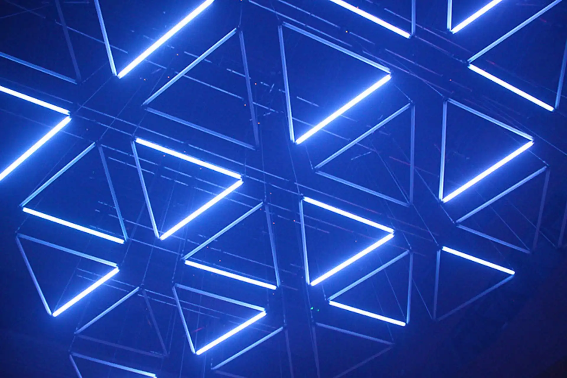 Detalle de techo luminoso en un evento, con tubos LED RGB 360 grados controlados por ArtNet. La estructura triangular azul crea un efecto visual futurista y sofisticado, ideal para eventos de alta tecnología.